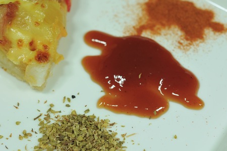 slice of pizza with ketchup, tomato sauce, oregano and dried chili pepper on a white plateの写真素材