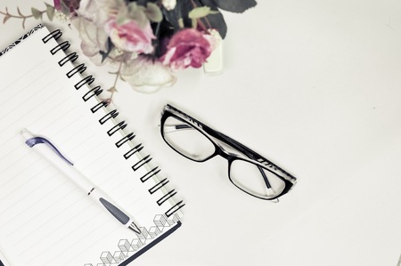 Top or flat lay view of eyeglass and notebook with flower decoration on white table background with copy space.の写真素材