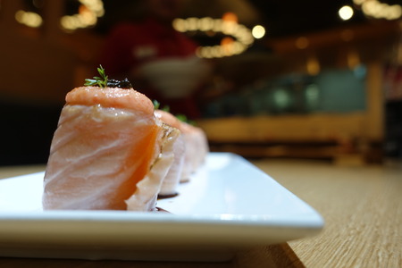 Close up of salmon rolls arranged on a white plate with a beautiful side dish, elegant, on the table in the restaurant. Blur background behind in the restaurant.の写真素材