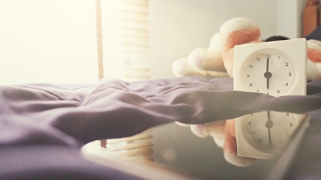 Alarm clock (6 o' clock in the morning) on the bed at home. Morning time background concept, soft focusing and vintage color style.の写真素材