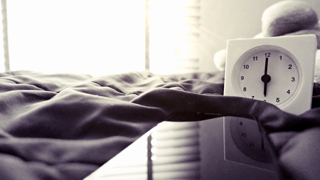 Alarm clock (6 o' clock in the morning) on the bed at home. Morning time background concept, soft focusing and vintage color style.の写真素材