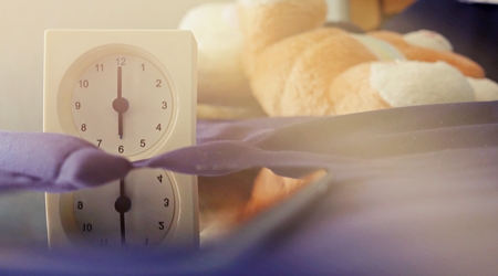 old memory time concept, retro square clock timed at 6 o'clock on the bed with sun light from windowの写真素材