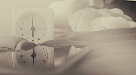 Alarm clock (6 o' clock in the morning) on the bed at home. Morning time background concept, soft...