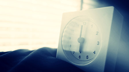 Alarm clock (6 o' clock in the morning) on the bed at home. Morning time background concept, soft...