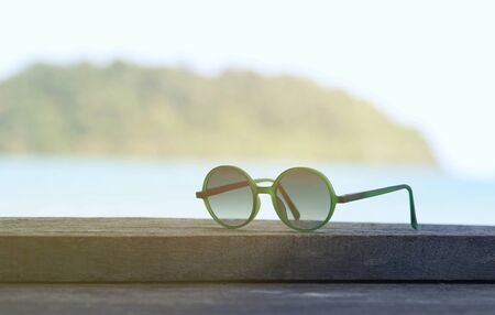 Sunglasses with sea and mountain view background, Fashion sunglasses on wood table with blue cloudy sky, Summer holiday. Beautiful Relaxing background. Copy space.の写真素材