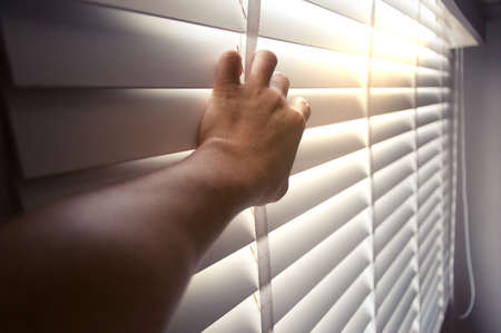 Windows jalousie. A man peeking through window blinds. Male hand separating slats of venetian blinds with a finger to see through with soft light. Clipping path included for design workの写真素材