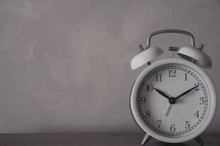 White alarm clock on wooden table and concrete wall background. Copy space.の写真素材