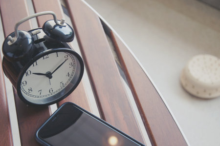 Alarm clock and mobile phone on wooden table in living room.の写真素材