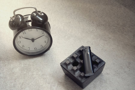 A black alarm clock and an empty black plastic box on a gray backgroundの写真素材