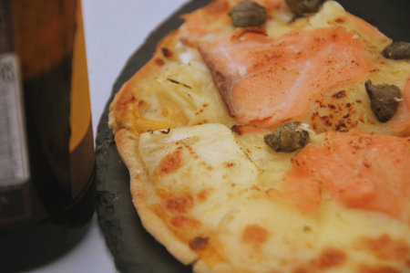 Pizza with salmon, cheese and spices on a black plate.の写真素材