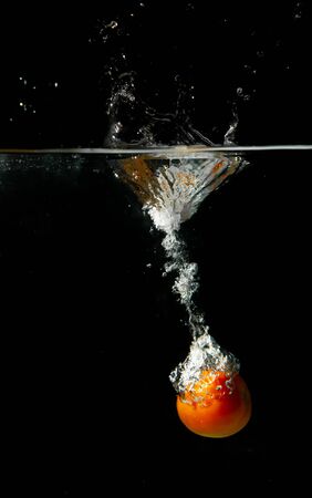 drop tomato in tank. water is splash on black backgroundの写真素材