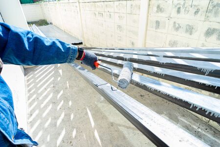 Worker painting steel tube with paint rollerの写真素材