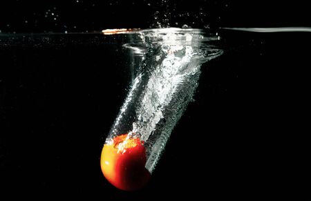 drop tomato in tank. water is splash on black backgrounddrop tomato in tank. water is splash on black backgroundの写真素材