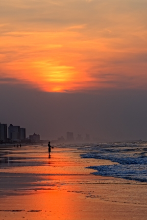 A silhouette os a lone fisherman fishing in the early morning in the Atlantic Ocean from the beach as the sun rises の写真素材