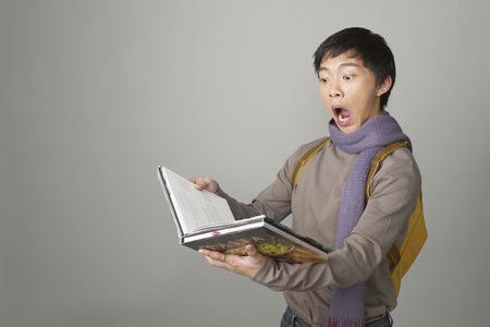 Young man opening mouth while reading bookの写真素材