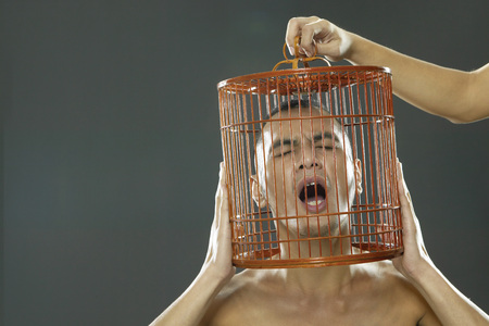 Young man shouting with head in birdcageの写真素材