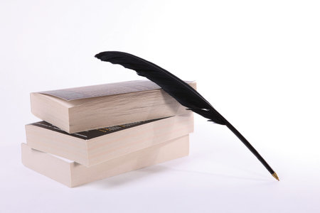Stack of books and black feather on white backgroundのeditorial素材