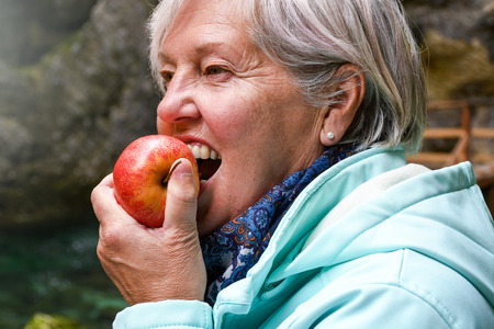 Healthy looking senior woman with grey hair eating apple outside in the parkの写真素材