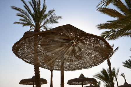 Sun rays shining through holes of wooden umbrella on the beachの写真素材