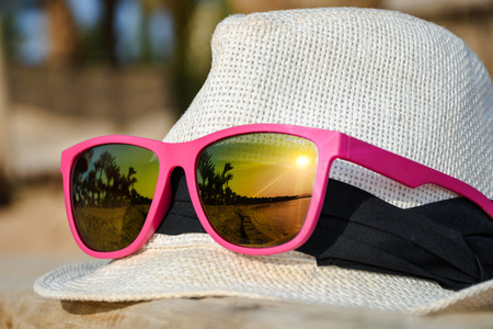 White hat on a wooden pier with fashionable pink sunglasses and reflectionの写真素材
