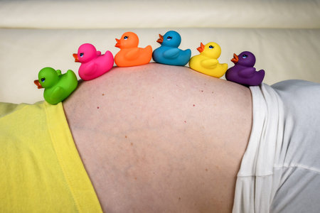 Pregnant woman wearing white bathrobe relaxing and resting at home on a white couch thinking and...