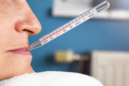 Close up of ill woman with flu and thermometer in her mouth measuring body temperature reaching 39 degrees celsiusの写真素材