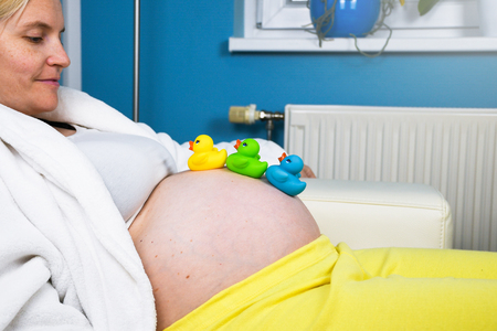 Pregnant woman wearing white bathrobe relaxing and resting at home on a white couch thinking and expecting her newborn babyの写真素材