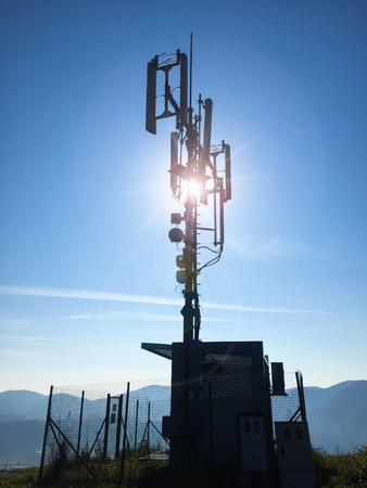 Silhouette of a high cellular telecommunication base station antennas on a sunny dayの写真素材