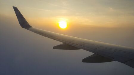 Wing of the aircraft looking from the airplane window and catching first sunset before going in to the cloudsの写真素材