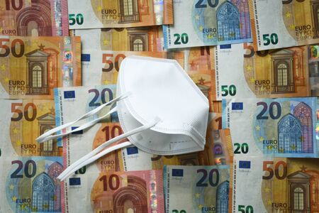 White protective medical face mask laying on the European union money currency Euro different paper notesの写真素材