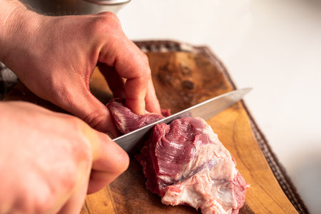 A man cuts red meat on a wooden board with a sharp knifeの写真素材