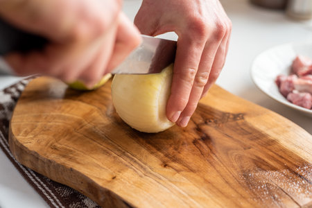 A man cuts onions on a wooden board with a sharp knifeの写真素材