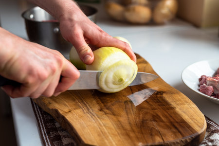 A man cuts onions on a wooden board with a sharp knifeの写真素材