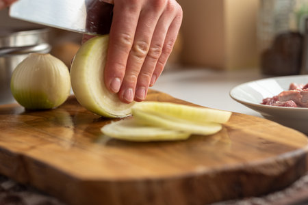 A man cuts onions on a wooden board with a sharp knifeの写真素材