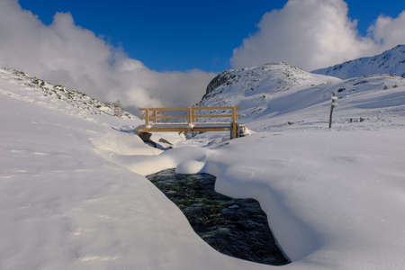Bridge over a mountain stream in winter. Winter mountain landscape. January in the Valley of Five Ponds in the Tatra Mountains. Blue sky over the valley.の写真素材
