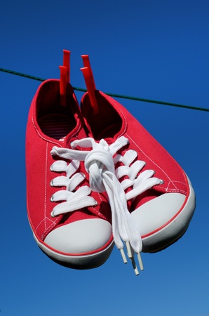 New sneakers with laces knotted together on washing line against blue skyの写真素材