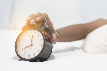 The girl sleeps in a white bed, handles the alarm clock.の写真素材