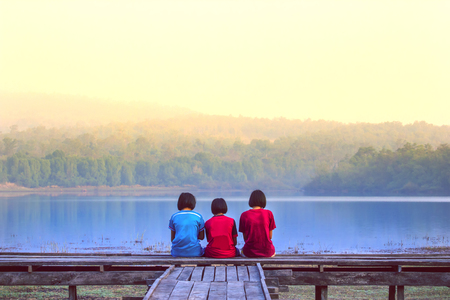 Three girls sitting on a bridge near the lake. Concept are friends.の写真素材