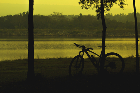 Black silhouettes, landscapes and mountain biking lean against trees along the lake.の写真素材