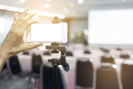 Mockup image blank screen of Modern smart phone. The hand of the operator controlling the mobile phone to record video in the meeting room.の写真素材