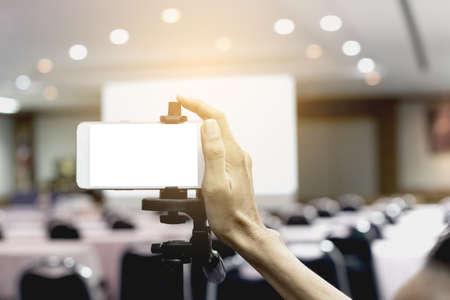 Mockup image blank screen of Modern smart phone. The hand of the operator controlling the mobile phone to record video in the meeting room.の写真素材