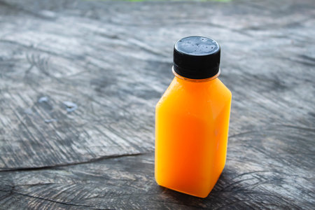 Cold fresh squeezed orange juice in a transparent plastic bottle with black lid placed on a wooden...