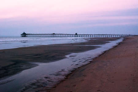 Pier in the distance at low tide with tracks in the sandの写真素材