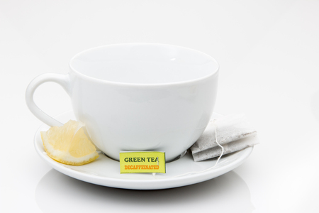 Green Tea bag on a saucer with a cup and lemon wedge.の写真素材