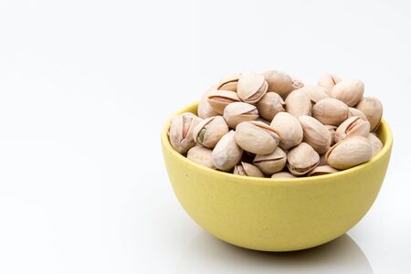 Pistachio nuts in a yellow bowl in a white bakcground.の写真素材