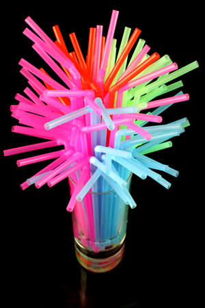 long drink glass with some water and many colored plastic straws symbolizing global water shortage on a black background の写真素材