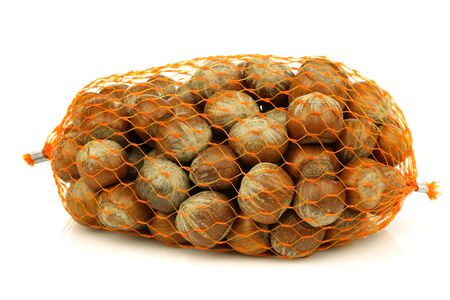 bunch of fresh hazelnuts in a plastic net on a white background の写真素材
