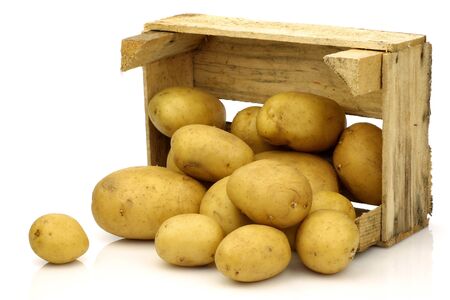 freshly harvested potatoes coming from a wooden box on a white background の写真素材