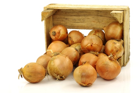brown onions coming from a wooden box on a white background の写真素材