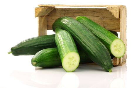 fresh cucumbers and a cut one in a wooden box on a white background の写真素材